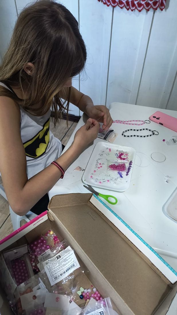 Adolescente montando um colar de miçangas na oficina de artesanato