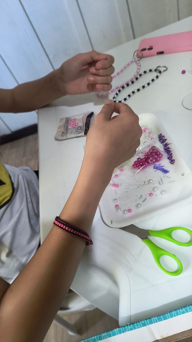 Mãos de uma adolescente enfiando miçangas em um fio durante a oficina