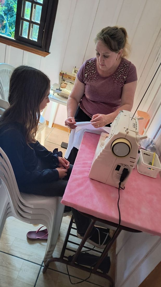 Voluntária ensinando uma adolescente a preparar o tecido para a costura