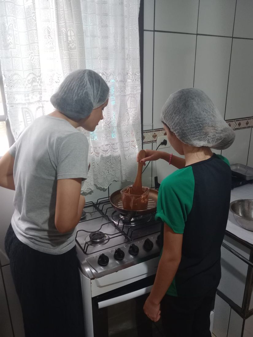 Duas adolescentes de touca derretendo chocolate no fogão durante a aula de culinária