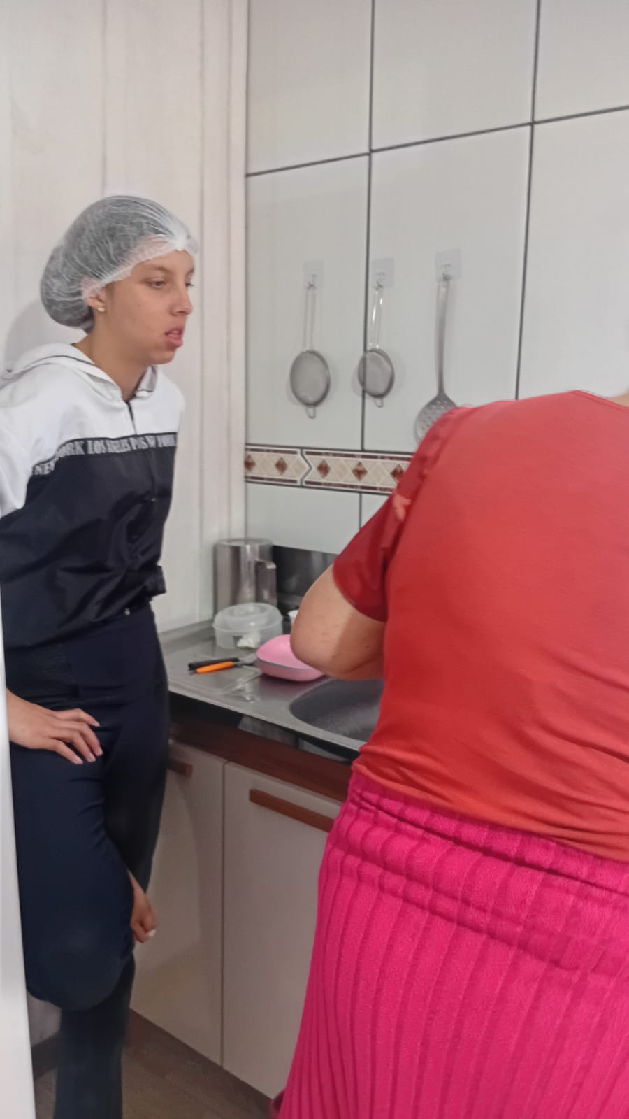 Adolescente de touca conversa com a voluntária durante o preparo na cozinha do projeto