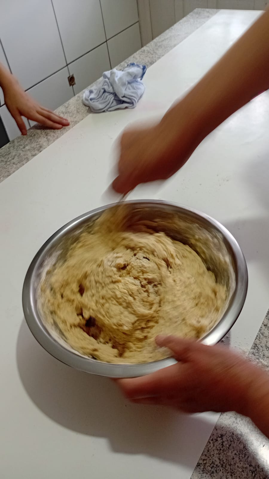 Mãos sovando a massa de pão dentro de uma bacia sobre a bancada da cozinha
