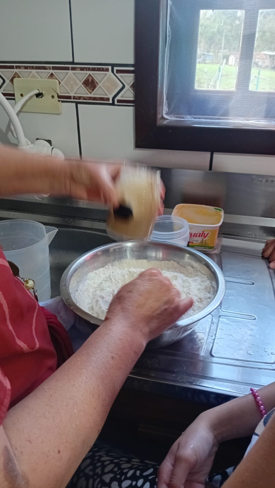 Voluntária despejando a mistura de fermento sobre a farinha enquanto as alunas acompanham